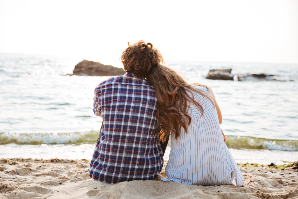 Beautiful young couple sitting together on the beach