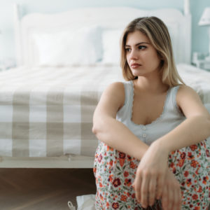 Depressed young woman sitting on bed at home