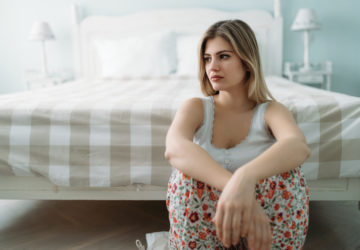 Depressed young woman sitting on bed at home