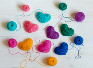 Multicolored Hearts with a balls of thread on white wooden background