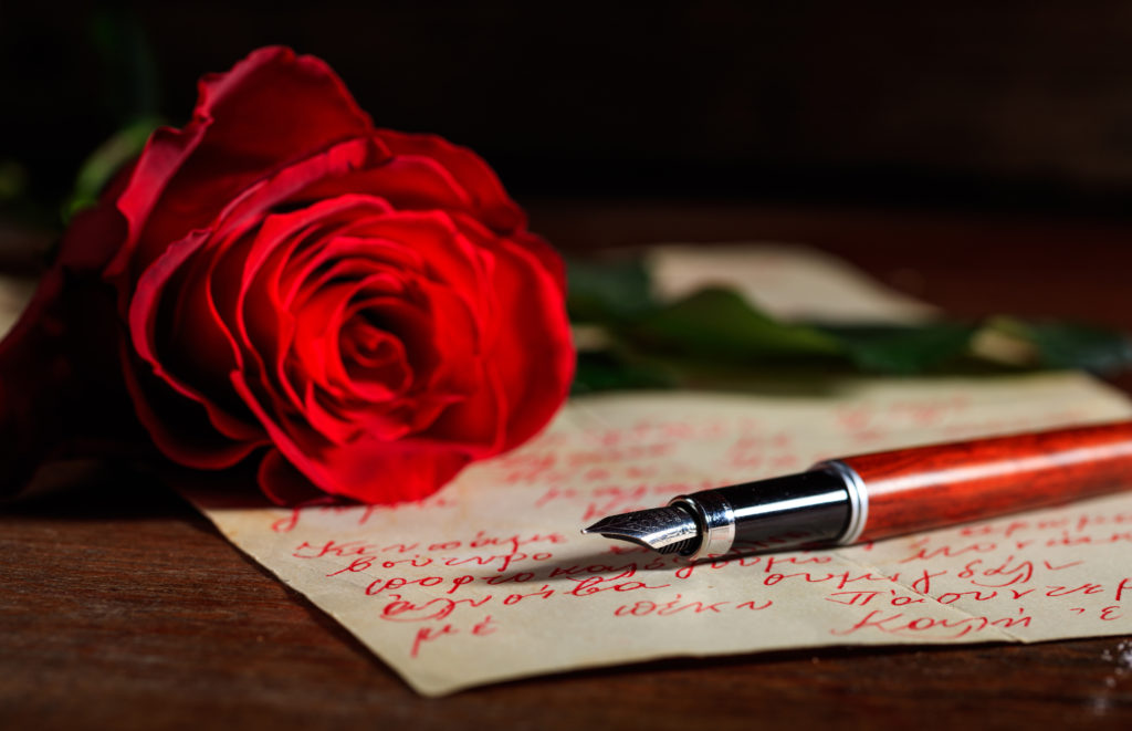 Red rose and an ink pen on a handwritten letter