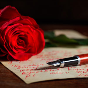 Red rose and an ink pen on a handwritten letter