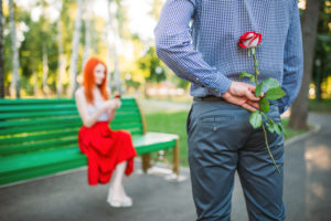 Woman sits on bench, man with rose stands against