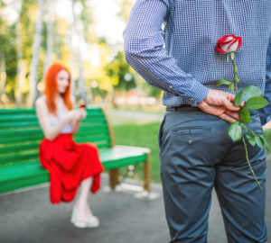 Woman sits on bench, man with rose stands against
