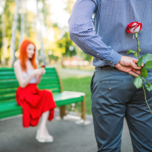 Woman sits on bench, man with rose stands against
