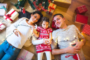 Young family lying under Christmas tree among presents