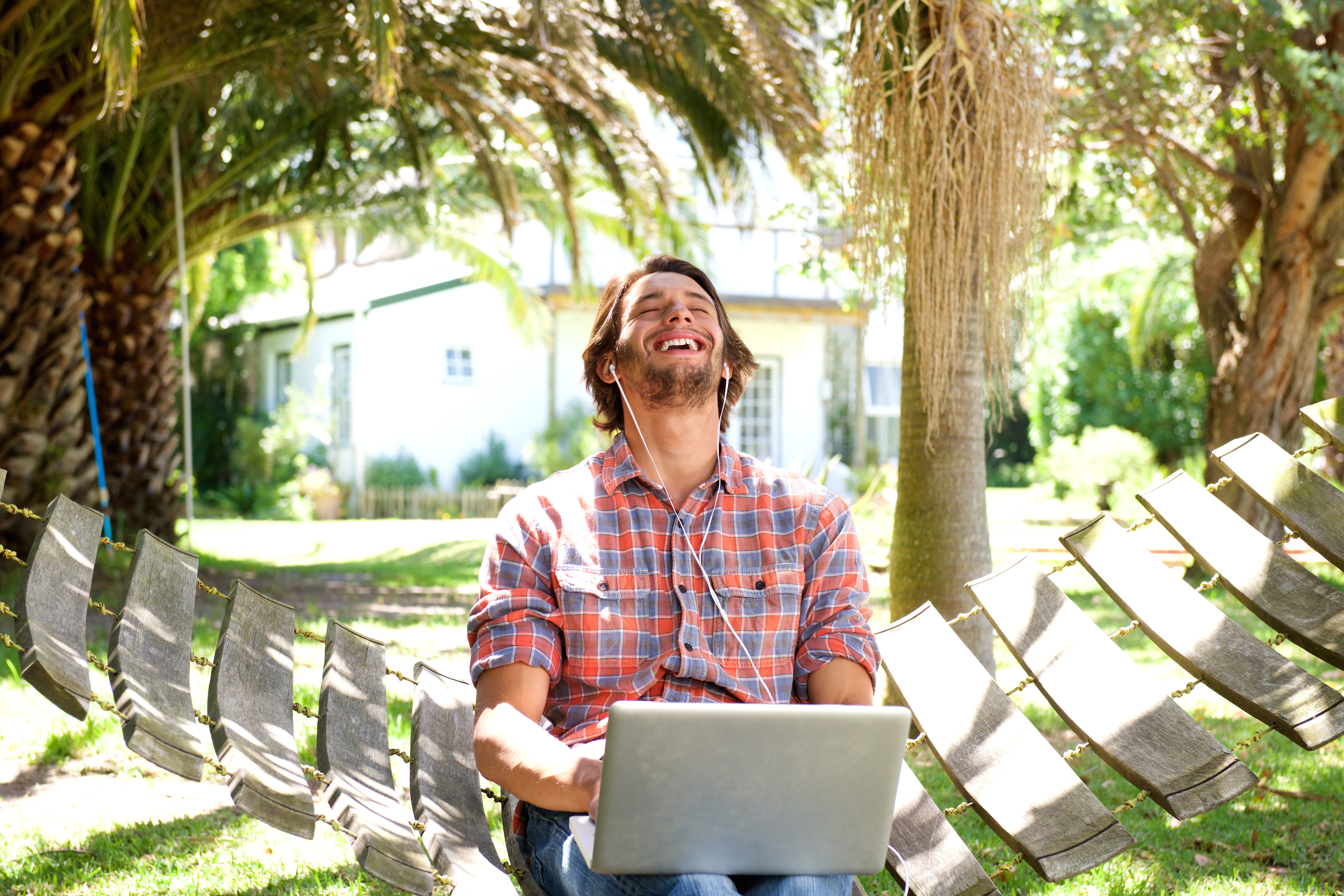 Young man laughing with laptop outdoors
