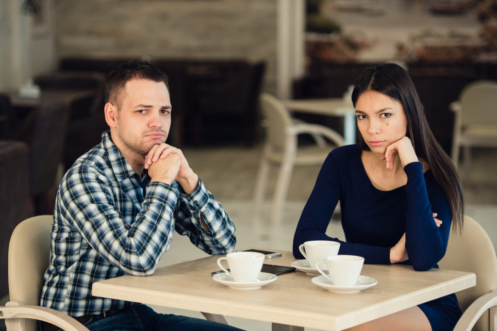 Young unhappy married couple having serious quarrel at cafe