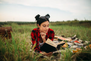 Young woman lies on plaid and reads book, picnic